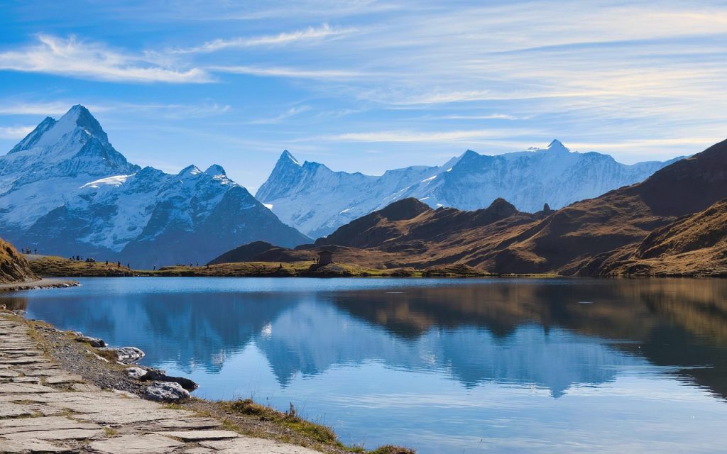 Snow-Capped Mountains Reflected in a Calm Lake Under a Clear Blue Sky
