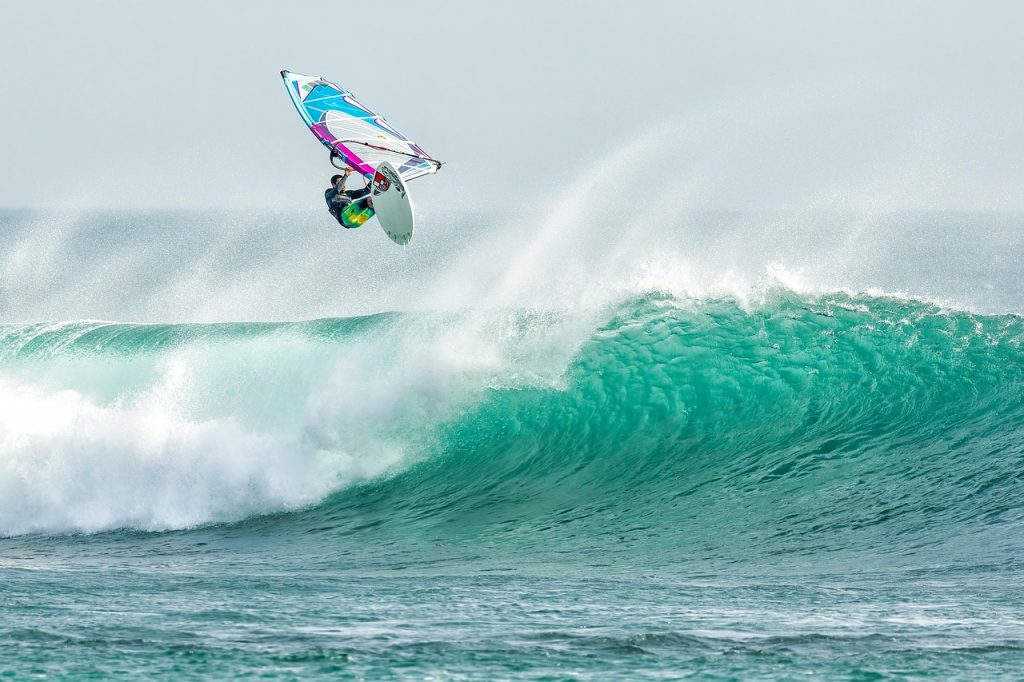 Windsurfer Performing an Aerial Trick Above a Large Turquoise Wave in the Ocean