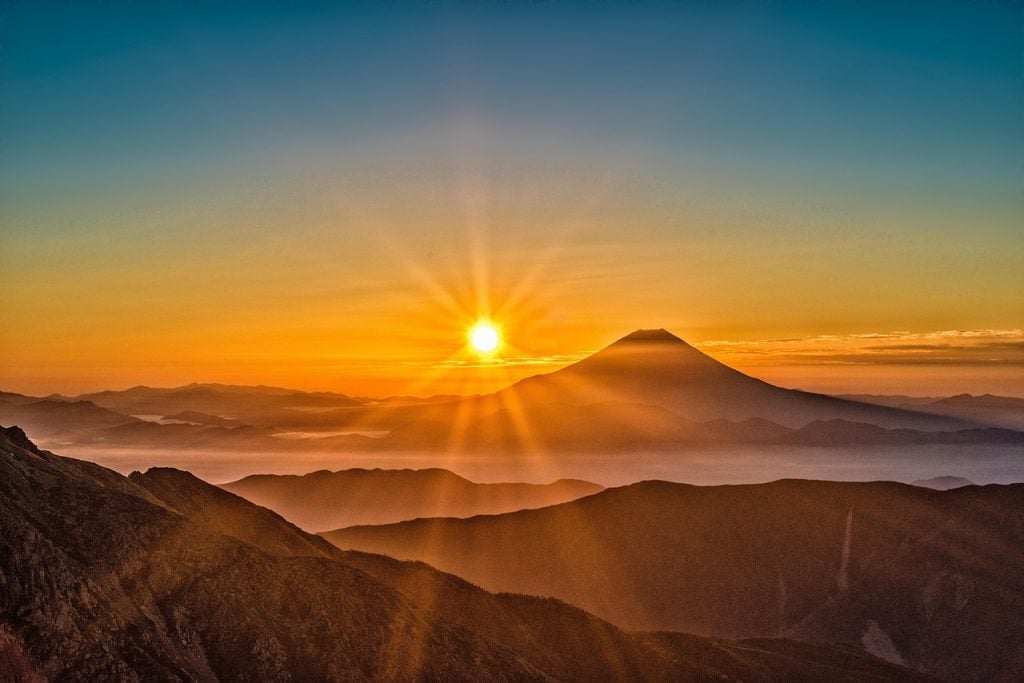 Golden Sunrise over Mountain Peaks with Mount Fuji Silhouette and Radiant Sun Rays
