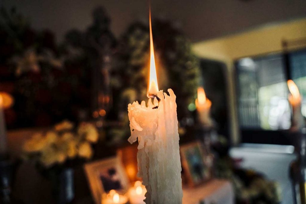 Lit White Memorial Candle With Wax Drippings In A Funeral Or Cremation Setting