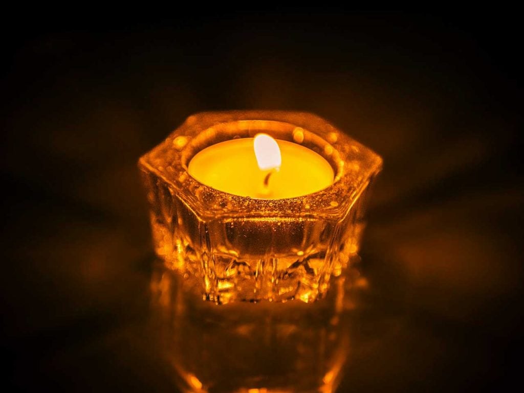 Glowing Memorial Candle In A Decorative Glass Holder Against A Dark Background